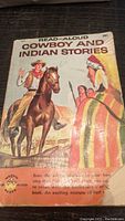 Close-up photo of the book's front cover showing the title, artwork of cowboy and Native American figures, and wear on the cover.