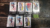 Seven sealed vintage 1990's Skybox basketball cards in clear chip bags arranged on wooden surface showing front images.