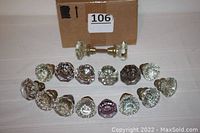 Photo showing all 16 glass and brass doorknobs arranged with box in background. Mix of clear and some light purple colors visible.
