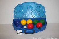 Open blue plastic case showing 8 bocce balls in red, green, yellow, and blue, plus a small white pallina target ball in center.
