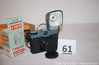 Diana-F 120 film camera with attached lens cap and Diana-F 162A flashlight, alongside the flashlight box