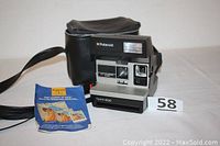 Polaroid Spirit 600 camera, carrying case, and user manual booklet displayed on a white surface, showing front and flash unit.