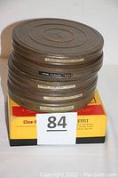 Stack of five metal 16mm film reels labeled with years and titles, placed on top of a yellow and black Cine-Kodak Duo Splicer box, with auction lot number visible.