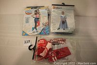 Packaged Harley Quinn and Colonial Village Girl costumes with M&M costume pieces on table.