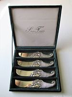 Four silver butter knives featuring detailed cornucopia design on the handles arranged in original green presentation case marked 'Silver Treasures by Godinger'.