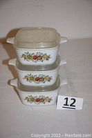 Stacked view of three Corning Ware storage containers with Splice of Life pattern showing plastic lids and floral fruit decoration on sides.