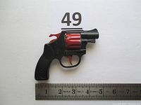 Black and red plastic toy revolver with ruler showing approximate length of 4.5 inches. Visible wear on red plastic parts.