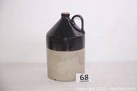 Side angle view of brown glazed top half and off-white bottom half stoneware jug with handle, no visible cracks.