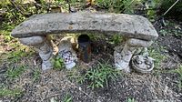 Concrete yard bench in garden setting with detailed stone texture and some discoloration, with sleeping dog and kitten lawn ornaments beneath