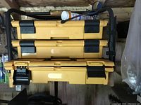 Three yellow DeWalt wall mounted toolboxes on a metal rack, stacked vertically with black latches and handles visible.