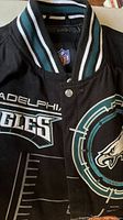 Front upper portion of the black Philadelphia Eagles jacket showing embroidered Eagles name and logo, with ribbed collar detail.