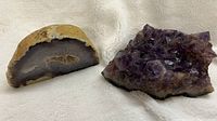 Two geode rocks displayed on a cream fabric background: a cut agate geode slice and an amethyst cluster.