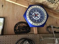 Hexagonal blue wall clock branded with Kobalt Tools logo, mounted on wooden wall with various tools and decor items around.