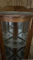 Curved front of the oak corner curio cabinet showing the upper glass shelf and wooden frame with lighting inside.