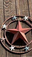 Close-up photo showing detail of large red three-dimensional star in center of metal ring with smaller painted stars on a wooden background.