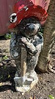 Front view of Paddington Bear composite outdoor statue showing red hat, face, body with paint wear, and shovel held by statue.