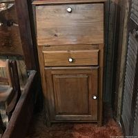 Front view of small wooden secretary desk with closed drop-front panel, single drawer, and cabinet door with white knobs.