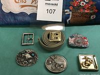 Lot showing five metal U.S. Marines belt buckles and one fabric belt with brass buckle.