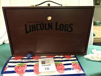 Open solid wood carry case with black printed "The Original Lincoln Logs" on lid interior and carry handle, showing off the storage space inside.