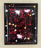 Frontal view of the graffiti style painting showing black framed artwork with red, white, pink, and gold splatters and motifs on black background.