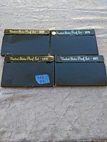 Four United States proof coin set cases for years 1976, 1977, 1978, and 1979 laid out showing front cover with year markings