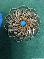 Clear top-down photo of the CORO gold tone brooch pendant showing intricate wire floral design with turquoise center on green background.