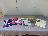 All eight vintage sheet music pieces displayed in a row on a table with a tape measure showing length of about 11-12 inches, colorful mid-20th century style covers.