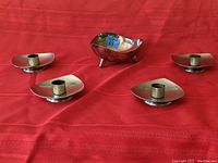Five piece set arranged on red fabric background, four candle holders surrounding a bowl, both made of sterling silver displaying mid century design.