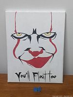 Full view of the painting showing Pennywise's face with red lines, yellow eyes, and the phrase 'You'll Float Too'