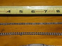 Top view of two sterling silver bracelets with measuring tape showing lengths approximately 7 inches and 6 inches respectively, placed on a wooden surface.