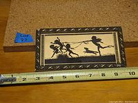 Full view of framed silhouette artwork showing figures and measurement tape indicating approximately 8 inches wide.