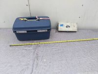 Side view of blue Samsonite bag and metal box with measuring tape showing length of bag approximately 14 inches.