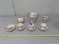 Full set arranged, showing teapot, sugar bowl, creamer, and four tea cup and saucer pairs with gold floral detailing.