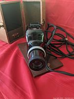 Black Kodaslide projector with power cord and base, placed on red cloth.