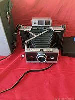Polaroid Land Camera Automatic 250 with bellows extended, front view showing lens, shutter button, and front panel details with carrying case in background.