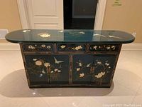 Front view of black lacquer console cabinet with three painted front drawers and two doors, paired with matching glass top