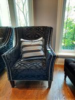 Front view of upholstered armchair with patterned fabric, nailhead trim, wood legs, and two accent cushions