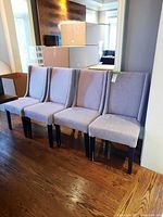 Four grey upholstered dining chairs with dark wood legs side by side on hardwood floor