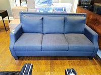 Front view of the blue fabric couch showing three seat and back cushions, nailhead trim, and wooden legs.