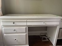 White wood desk front view showing the top drawers and seating area with space for legs and keyboard pullout.