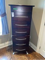 Front view of tall wood dresser with seven drawers, top drawer different knob handle, bottom drawer open and misaligned.
