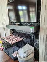 Wood fireplace mantle mounted on wall with black matte finish and slight curved side supports. Images show mantle in place with TV mounted above and pet crate below before removal.