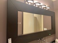 Front view of large framed rectangular mirror mounted on wall below light fixtures.