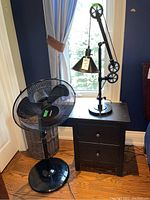 Desk lamp and floor fan positioned together on wooden floor beside window
