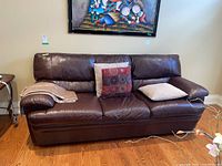 Front view of three-seat brown leather couch with two pillows and a throw blanket