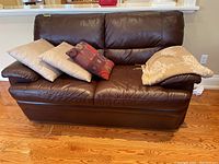 Front view of dark brown leather loveseat with three throw pillows and folded throw blanket