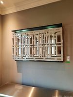 Front view of large wall mirror mounted on wall showing modern geometric white overlay on mirrored surface and black frame.