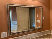 Front view of large rectangular mirror with detailed faux wood silver frame hanging on wall.