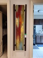 Front view of tall rectangular abstract print with wood frame side pieces, showing the colorful textured design dominated by red and gold hues.