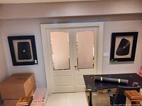 Two matching sculptural prints in black float frames mounted on wall above door.